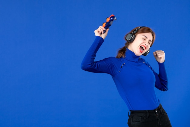 front view female gamer with gamepad and headphones on blue background joy player winning joyful online youth virtual winner video