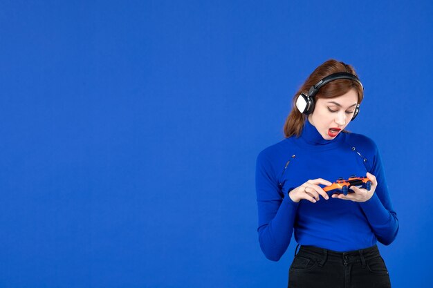 front view female gamer with gamepad and headphones on blue background player winning adult winner joyful video youth virtual joy