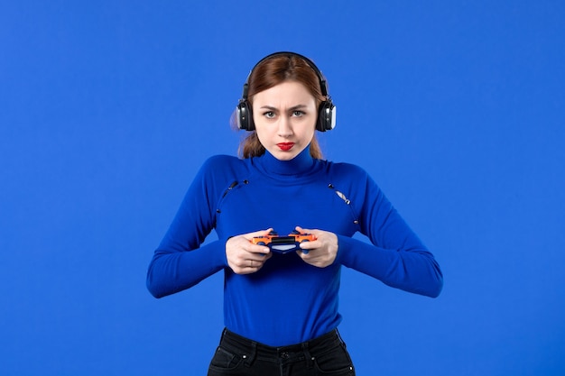 front view female gamer with headphones and gamepad playing video game on blue background player girl youth winning video virtual joy young adult