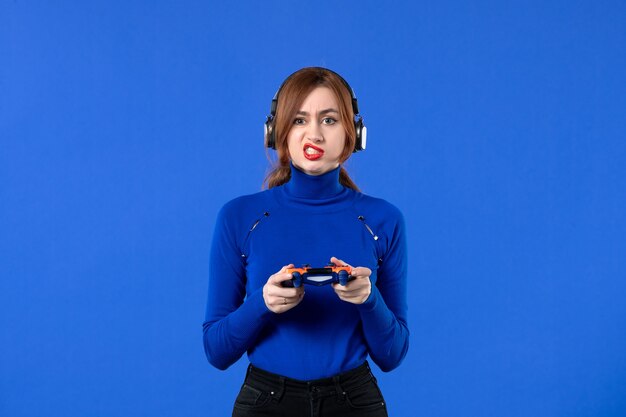 front view female gamer with headphones and gamepad playing video game on blue background youth sofa joy adult player girl winning