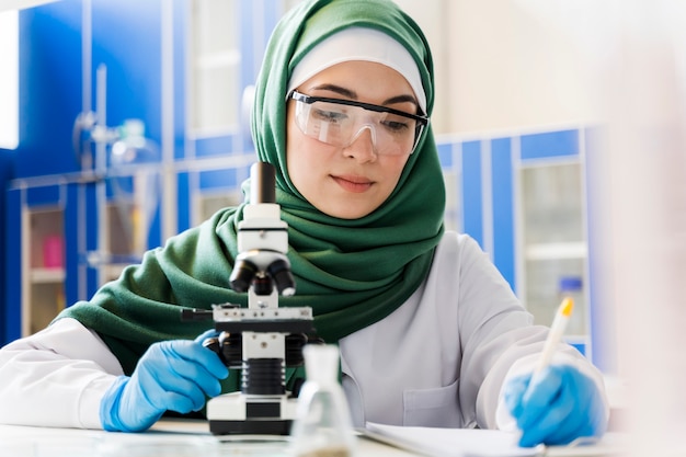 Vista frontale della scienziata con hijab e microscopio