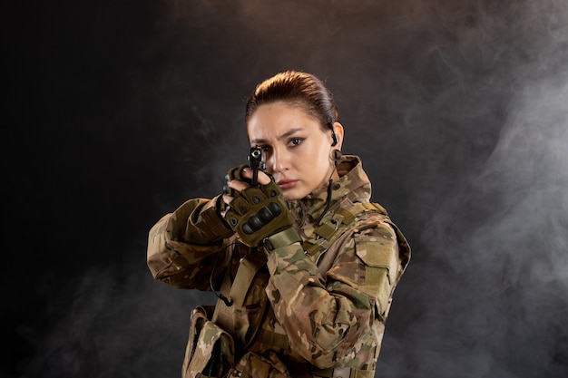 Front view of female soldier aiming gun in uniform on black wall
