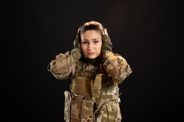 Front view of female soldier in camouflage on the black wall