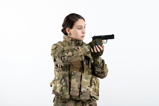 Front view female soldier in camouflage with gun on white wall