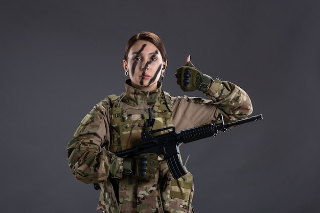 Photo front view female soldier in camouflage with machine gun on gray wall