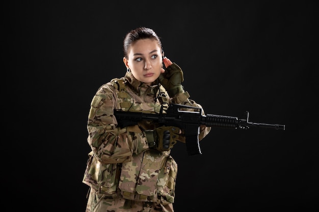 Front view of female soldier in uniform with rifle on a black wall