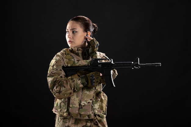 Front view of female soldier in uniform with rifle on the black wall