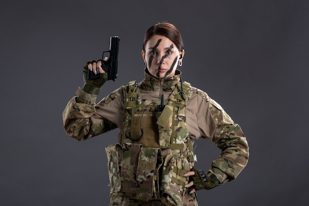 Front view of female soldier with gun in camouflage dark wall