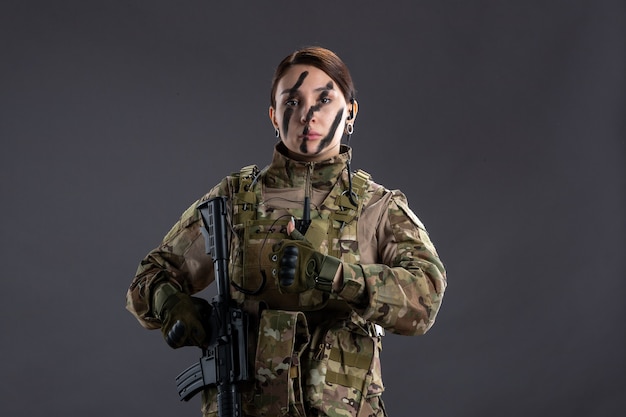 Front view female soldier with machine gun in camouflage dark wall