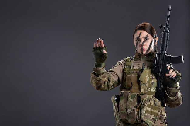 Photo front view female soldier with machine gun in camouflage dark wall