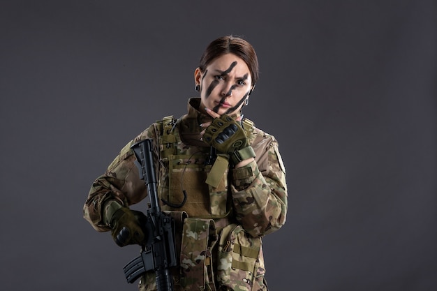 Front view female soldier with machine gun in camouflage dark wall