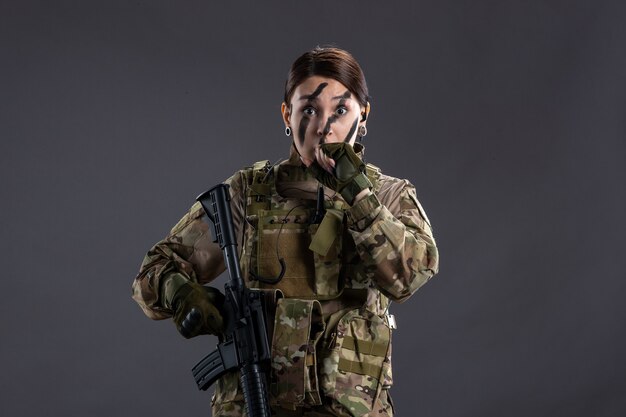 Front view female soldier with machine gun in camouflage on gray wall