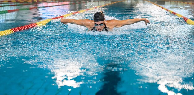 競争でストロークを実行するバタフライ スタイルを泳ぐ女子水泳選手の正面図