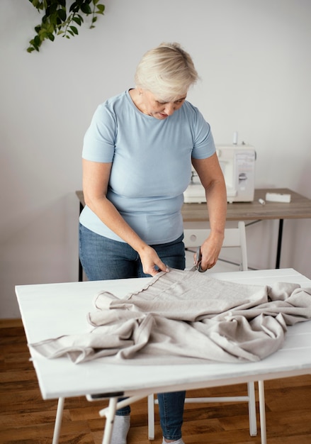 Photo front view of female tailor in the studio cutting fabric