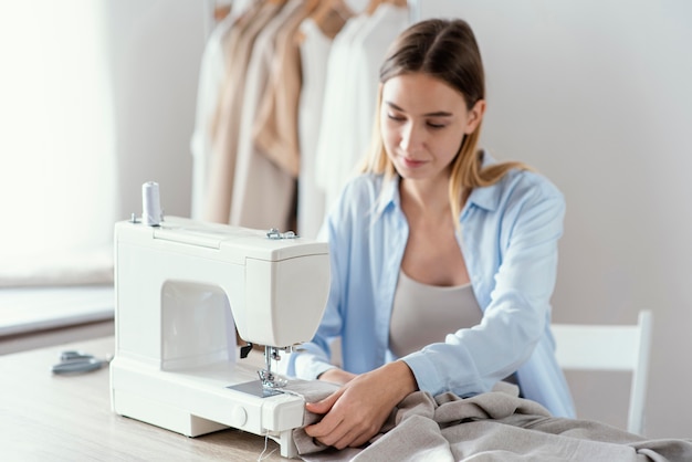 Photo front view of female tailor using sewing machine in the studio