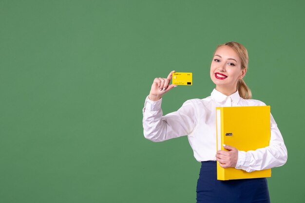 Front view female teacher holding yellow files and bank card on green