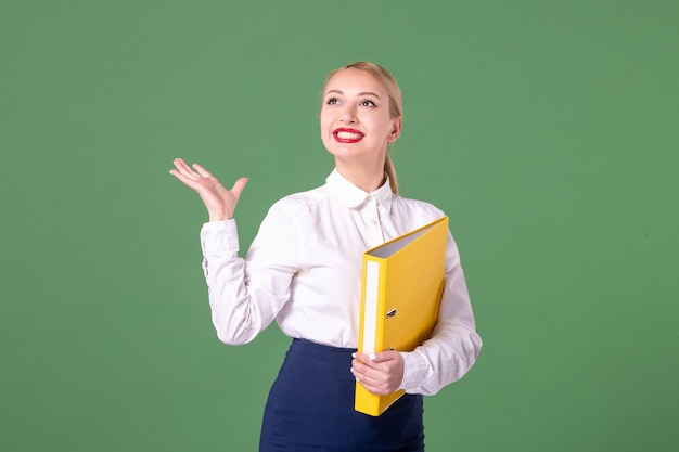 Front view female teacher posing in strict clothes with yellow files on green background work student book school woman lesson university library