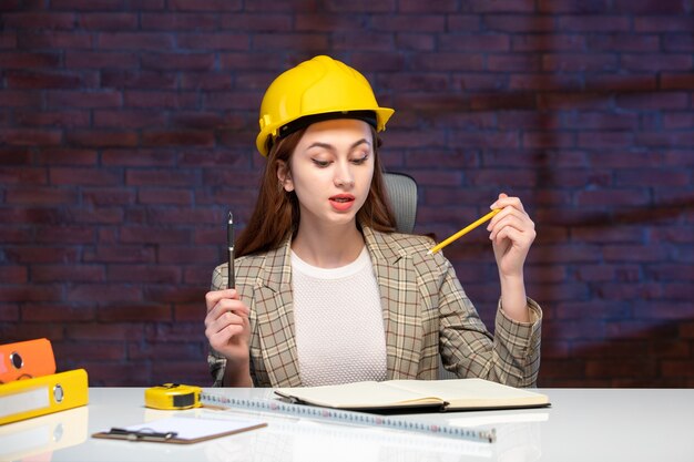 front view female worker in construction site sitting behind table with yellow helmet agenda job engineer business manager corporate plan working