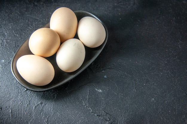 Vista frontale uova di gallina fresche all'interno della piastra su sfondo scuro torta di pasta colazione mattina colori tè pane latte