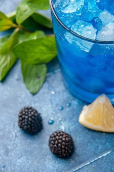 Vista frontale fresca fresca limonata all'interno di un piccolo bicchiere con ghiaccio su sfondo blu acqua fredda succo bevanda frutta color bar
