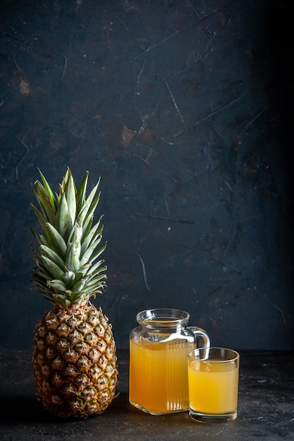 front view fresh pineapple juice in glass and carafe on dark background with copy space