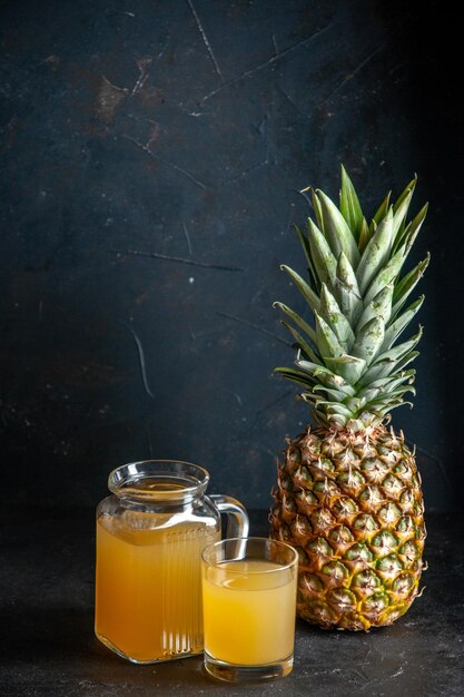 front view fresh pineapple juice in glass and carafe on dark background