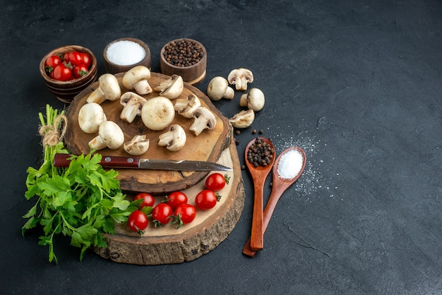 Front view of fresh raw mushrooms and green bundle knife tomatoes spices on wooden board towel on black background