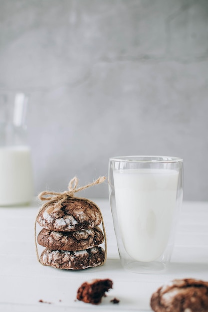 Foto vista anteriore di biscotti al cioccolato appena cotti e bicchiere di latte su un tavolo di legno rustico sopra il grigio