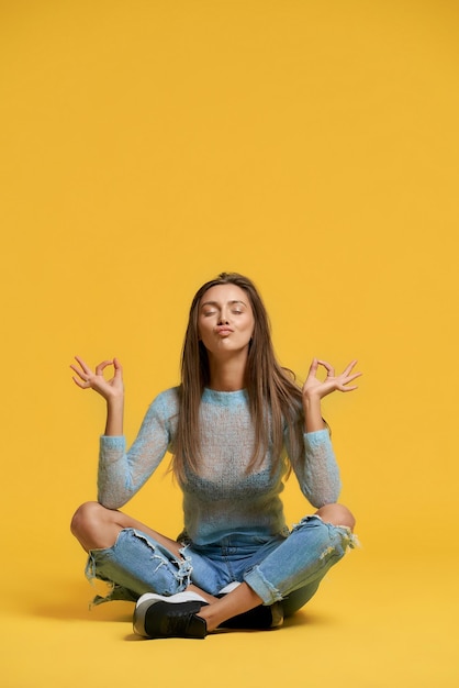 Front view of girl showing peace using lotus pose stylish pretty brunette woman sitting on floor