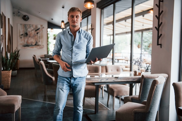 Front view of guy that is in modern cafe with his laptop at daytime.