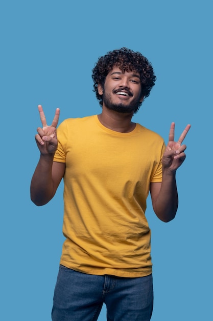 Front view of a guy with a toothy smile with raised forefingers and middle fingers posing for the camera