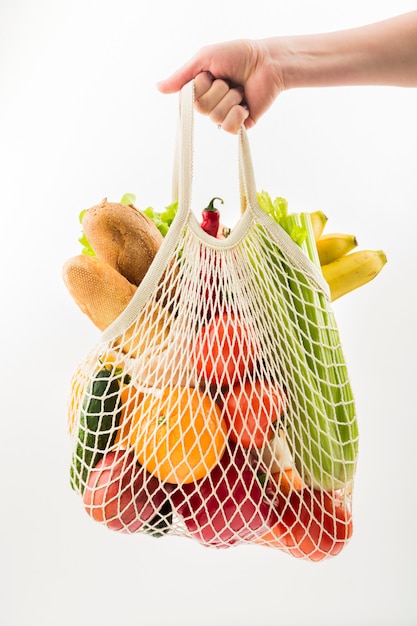 Front view of hand holding reusable bag with vegetables and fruit