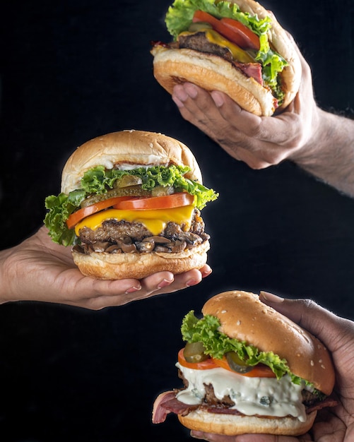 Front view hand holding three burgers dark back ground