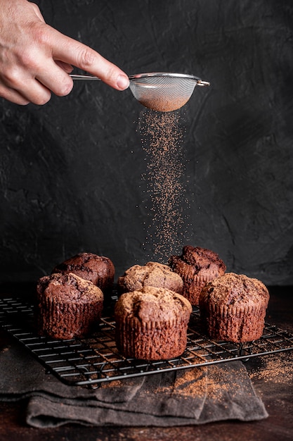 Foto vista frontale della mano che setaccia cacao in polvere sopra i muffin al cioccolato