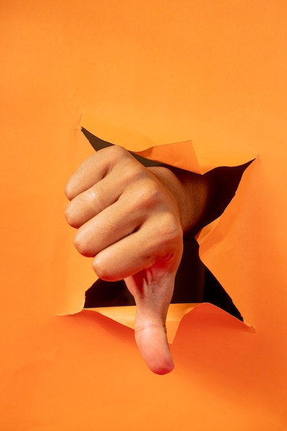 Front view of hands showing thumbs down out of orange torn paper background