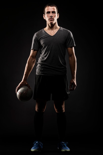 Photo front view of handsome male rugby player holding ball