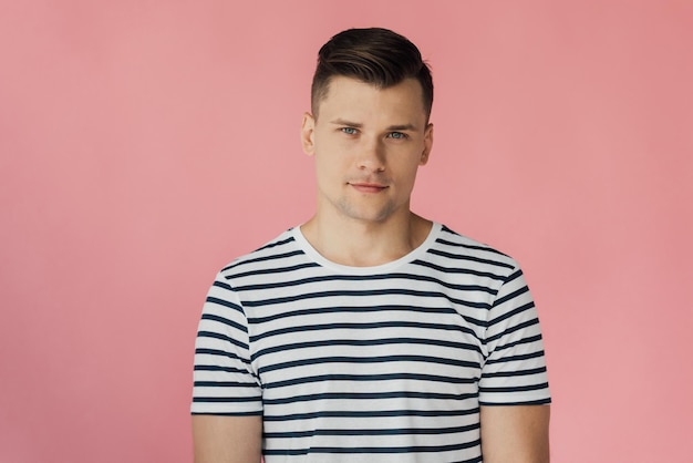 Front view of handsome man in striped tshirt looking at camera isolated on pink