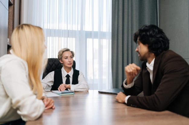 Foto vista anteriore di una giovane coppia felice che firma i documenti con il consulente finanziario nella pianificazione dell'ufficio dell'agenzia