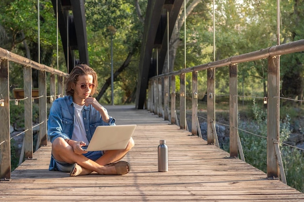 Front view of hipster young man working as digital nomad with
laptop sorrounded by nature