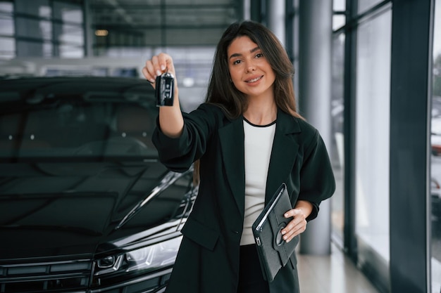 front view holding keys saleswoman in car showroom selling automobile