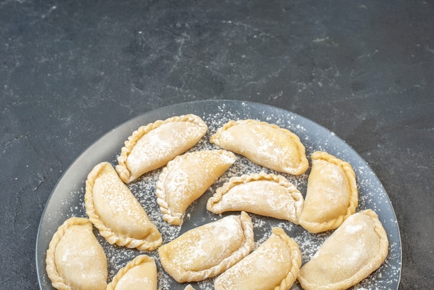 Front view of homemade raw dumplings on a plate on the bottom on black wall