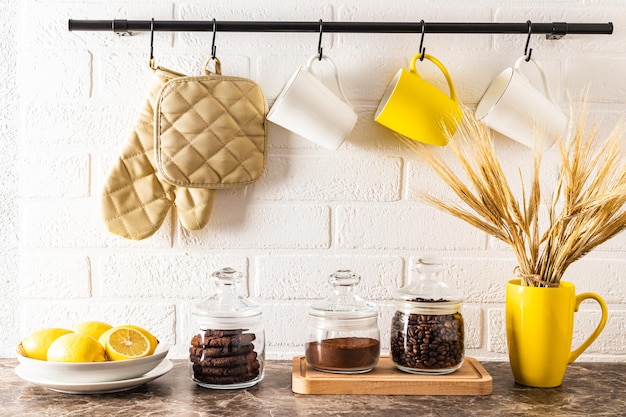 Front view of the kitchen marble countertop with cans of coffee and a bowl of lemons kitchen rail with mugs on a white brick wall