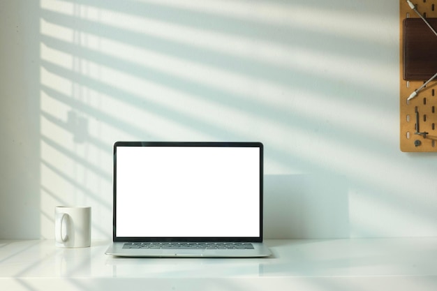 Front view of laptop computer and coffee cup on table with shadow from the jalousie on a white wall