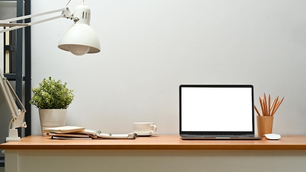front view of laptop potted plant lamp and supplies on wooden desk blank screen for text information or content