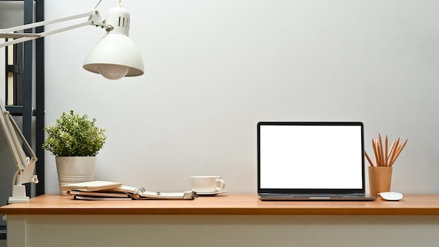 Front view of laptop potted plant lamp and supplies on wooden desk Blank screen for text information or content