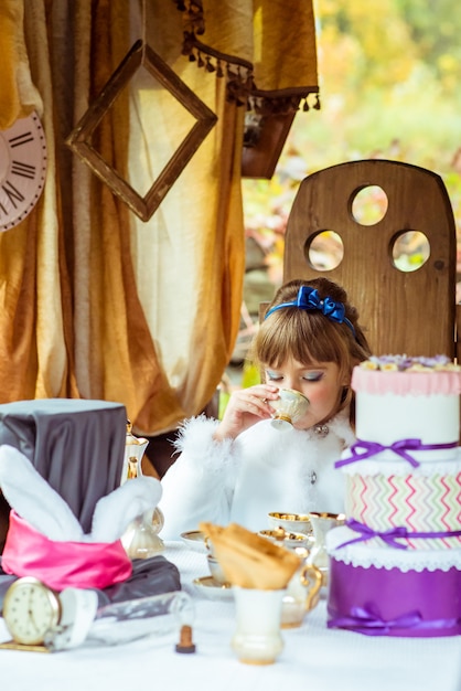 Front view of an little beautiful girl in the scenery drinking a tea at the table in the park