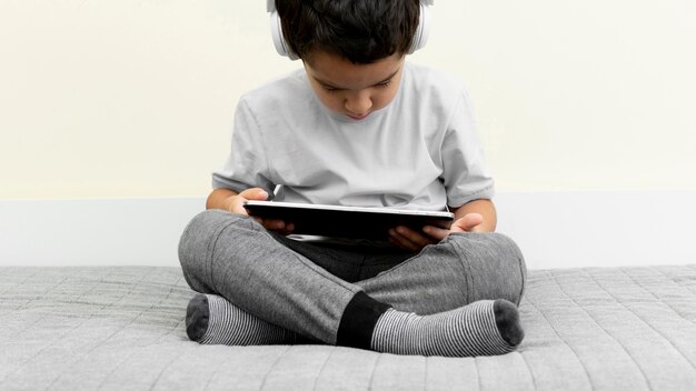 Photo front view of little boy using tablet in bed