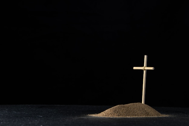 Front view of little grave from sand with stick cross on black