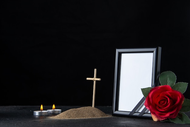 Front view of little grave with cross and picture frame on dark