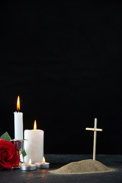 Front view of little grave with red rose and candles on\
black